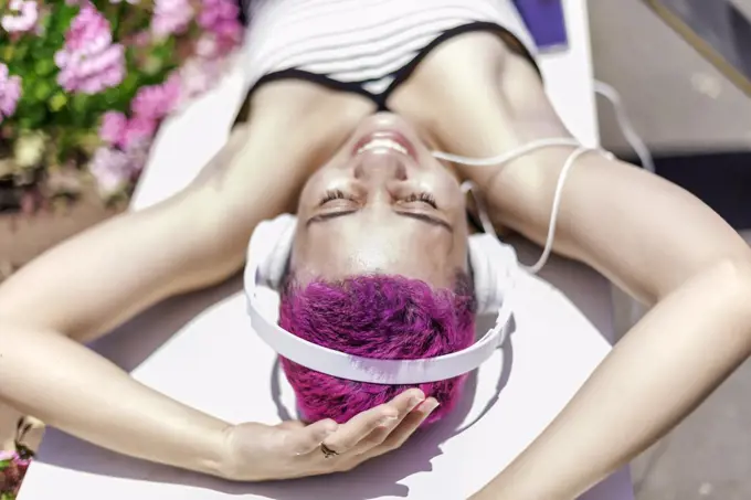 Woman with purple hair and headpones is listening music in her mobile
