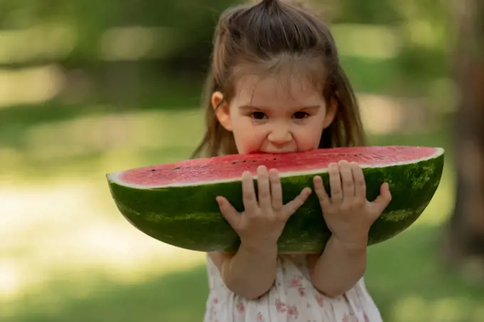 Pretty little girl bitting big piece of juice watermelon
