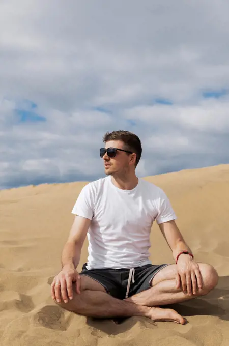 Man in sunglasses sitting in lotus pose in desert on sand