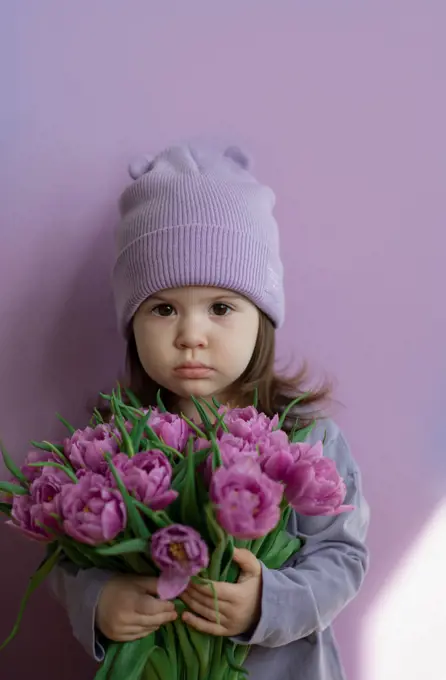 Pretty baby toddler wearing purple with bouquet of tulips.