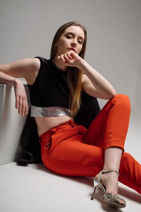 Woman model dressed in red trousers and black jacket posing in studio