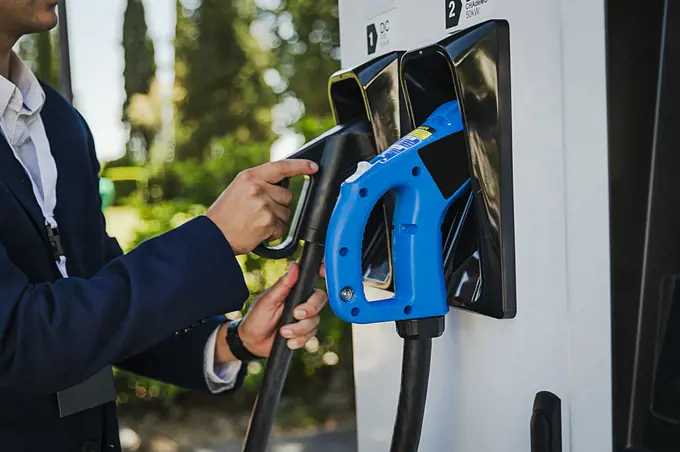 Businessman in a suit refueling his vehicle with an electric charger