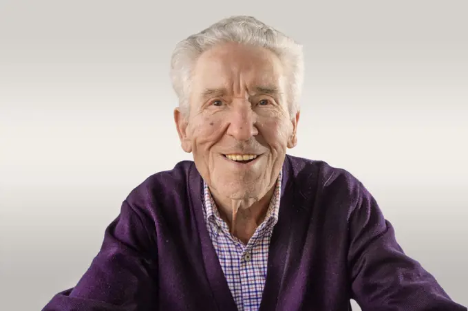 90 year old man in purple sweater looking at camera happy