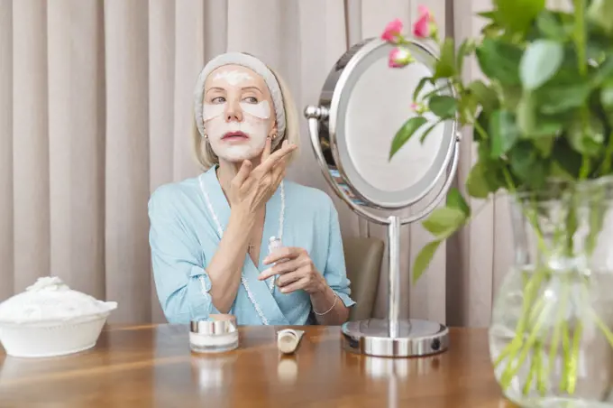 A mature woman uses a moisturizing cosmetic face mask.