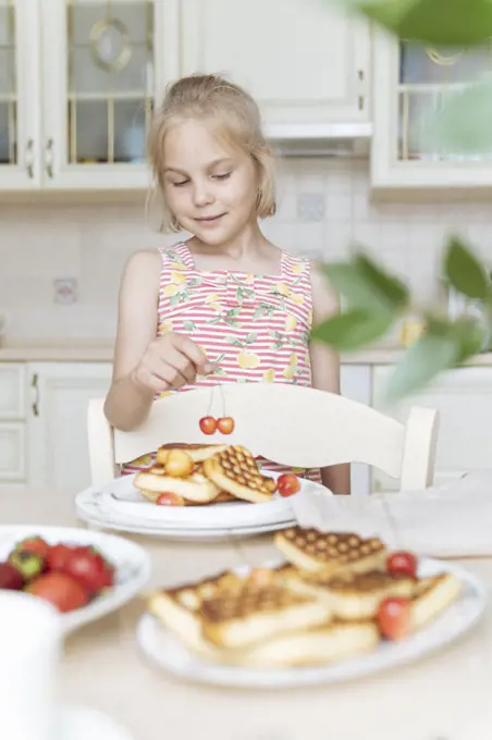 The girl cooks herself a breakfast of waffles and cherries.