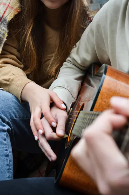 the hands of a girl and a boy on a guitar