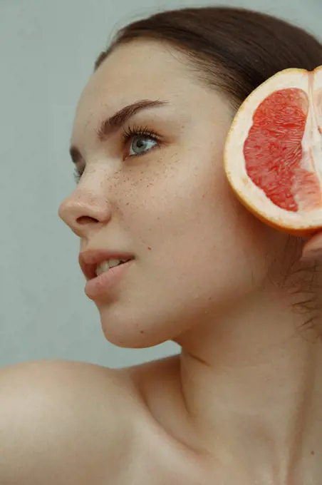 Close-up portrait of a young woman with freckles and half a grapefruit