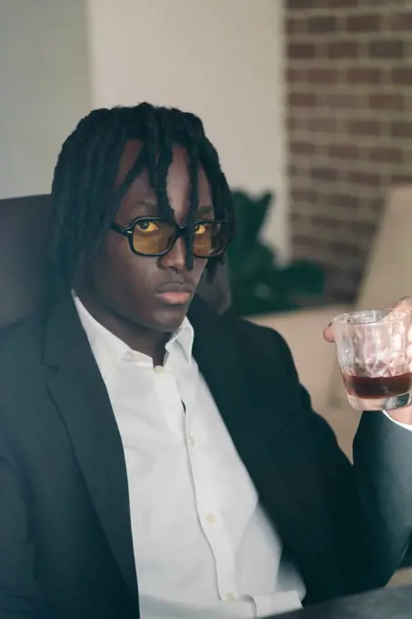 Black man with dreadlocks wearing a suit having a drink
