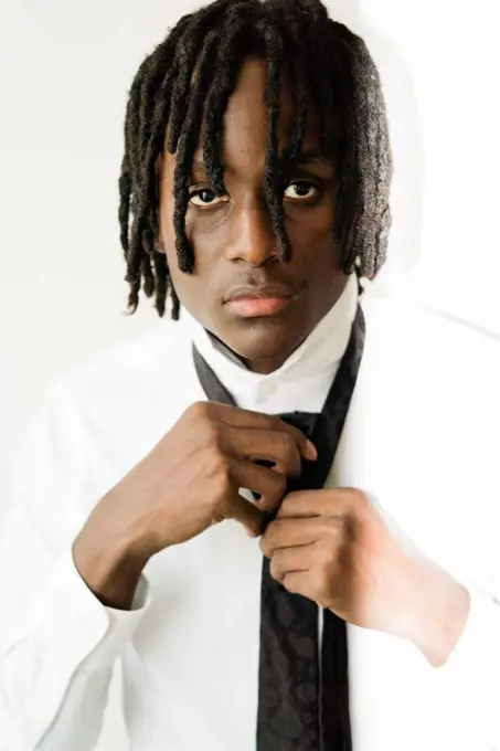 Black man with dreadlocks wearing a suit fixing his tie