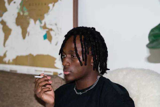 Black man with dreadlocks sitting on the sofa smoking
