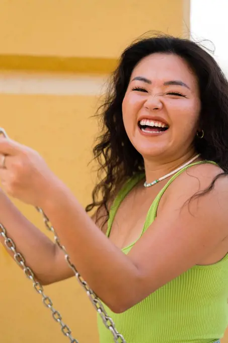 Asian woman sitting on the swings against yellow wall background