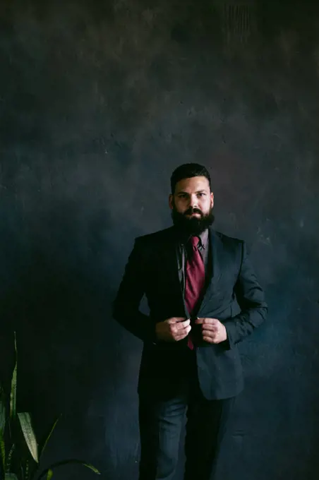 Portrait of attractive young bearded man in suit on dark background