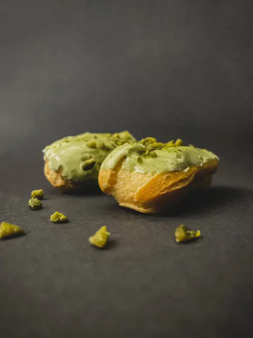 Two pistachio eclairs on dark background with pistachio pieces