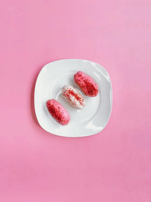 White and pink eclairs on top of a white plate on pink background