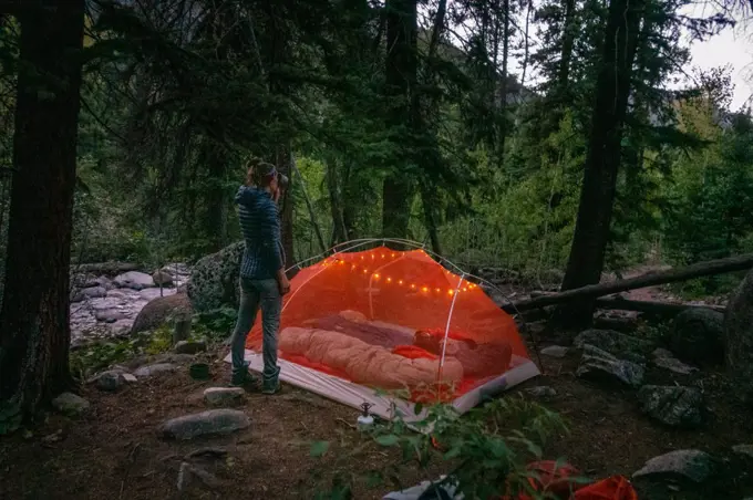 Woman drinking water by tent, camping at night.