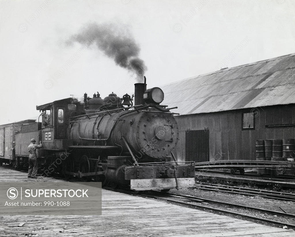 Stock Photo: 990-1088 Rear view of a man standing beside a steam train engine at a railroad station